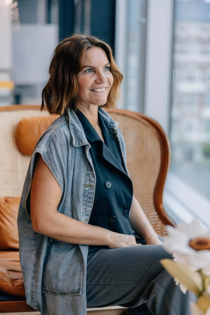 Mathilde Holmer sitting in a rattan chair by a window, smiling